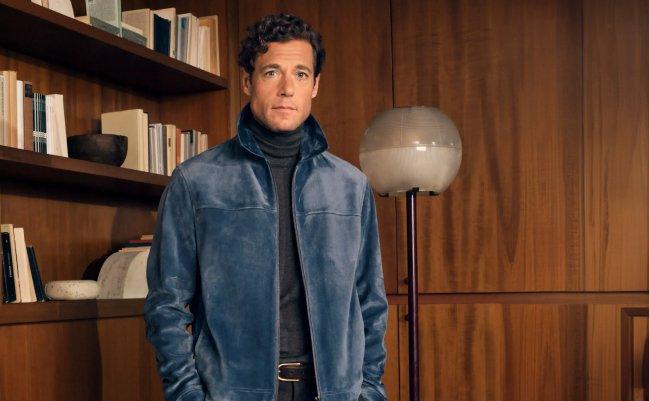 Un homme portant une veste en gabardine bleu marine foncé, accompagnée d’une chemise blanche à col et d’un pantalon de couleur claire