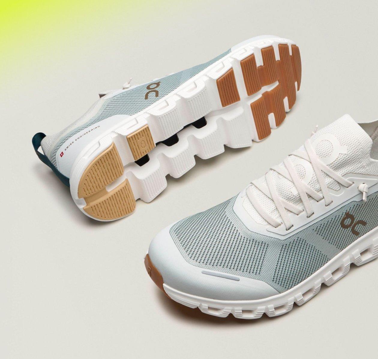 A pair of running shoes, featuring a light grey mesh upper, white laces, and a distinctive cushioned sole with a tan and white tread pattern