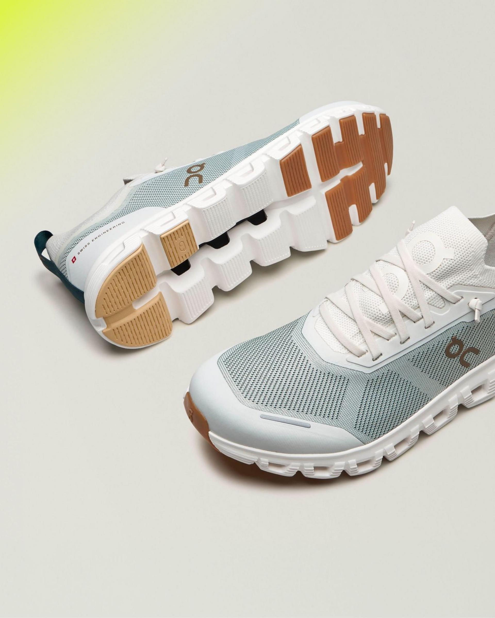 A pair of running shoes, featuring a light grey mesh upper, white laces, and a distinctive cushioned sole with a tan and white tread pattern