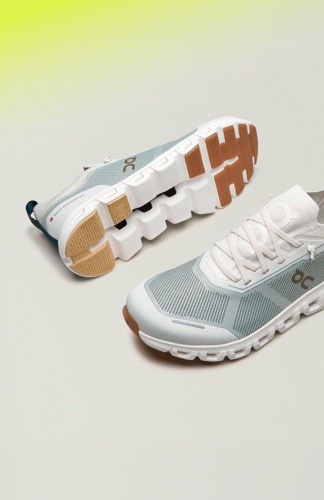 A pair of running shoes, featuring a light grey mesh upper, white laces, and a distinctive cushioned sole with a tan and white tread pattern