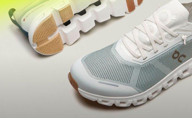 A pair of running shoes, featuring a light grey mesh upper, white laces, and a distinctive cushioned sole with a tan and white tread pattern