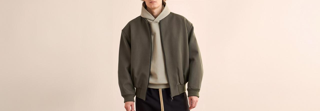 Un homme portant un hoodie beige superposé à une veste vert olive avec un pantalon cargo noir