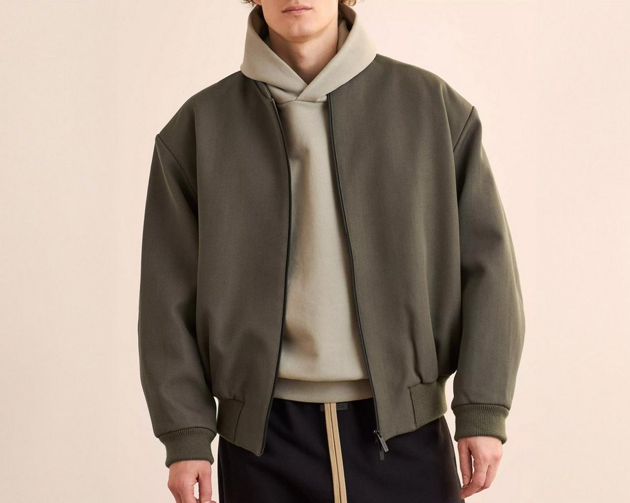 A man wearing a beige hoodie layered over an olive green jacket with black cargo pants