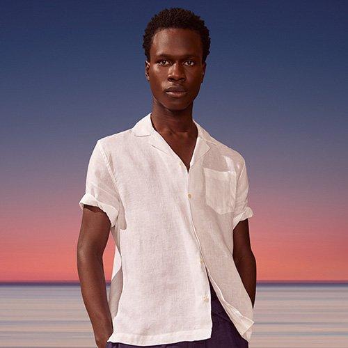 A man in white shirt standing on a beach with a sunset in the background