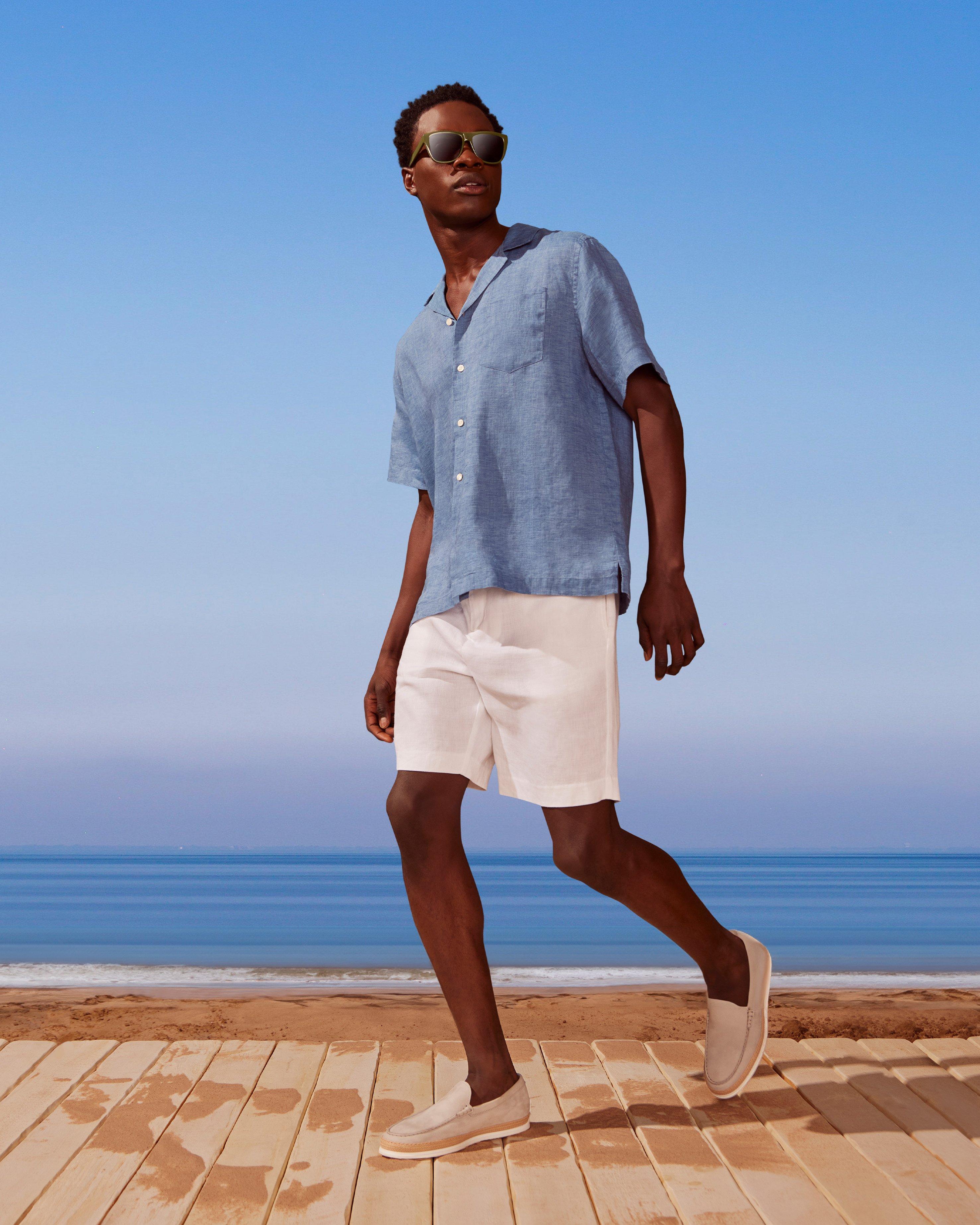 A man in a blue shirt and white shorts walking on a beach