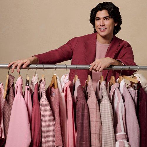 Un homme debout à côté d’un portant de vêtements avec des chemises roses et rouges