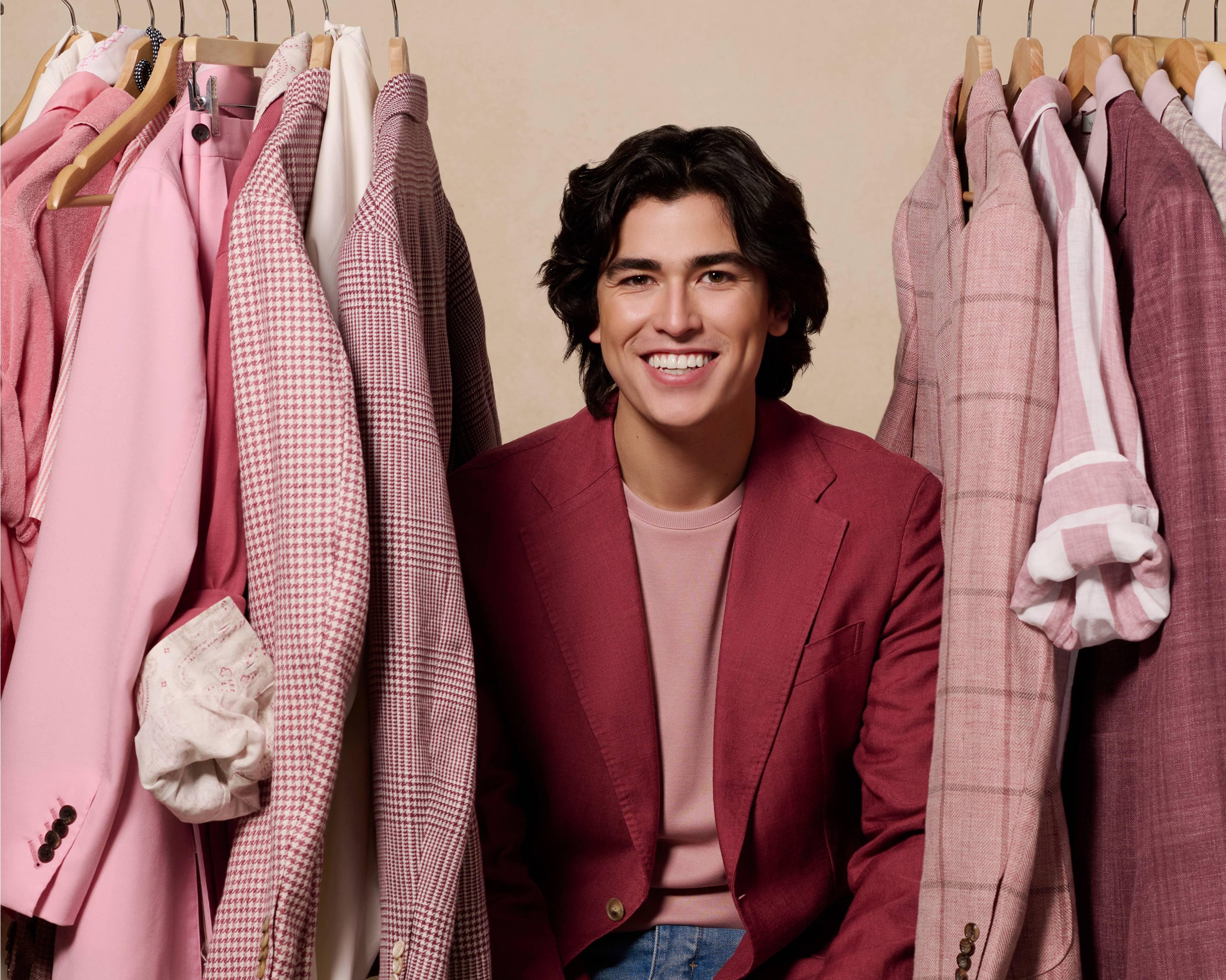 A man in a red jacket sitting in front of a rack of clothes