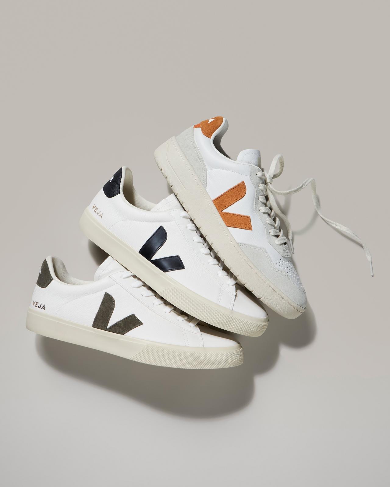 Three white VEJA sneakers with orange and black stripes on them