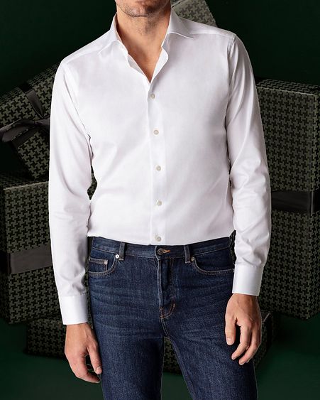 Male model showcases white shirt and blue jeans against dark green background