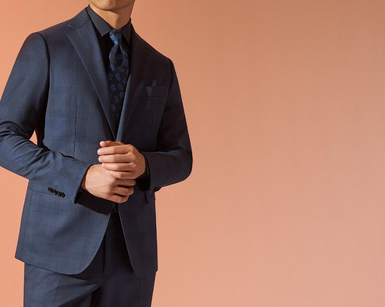 A close up of a male model wearing a navy fine tailored suit paired with a black and navy paisley tie