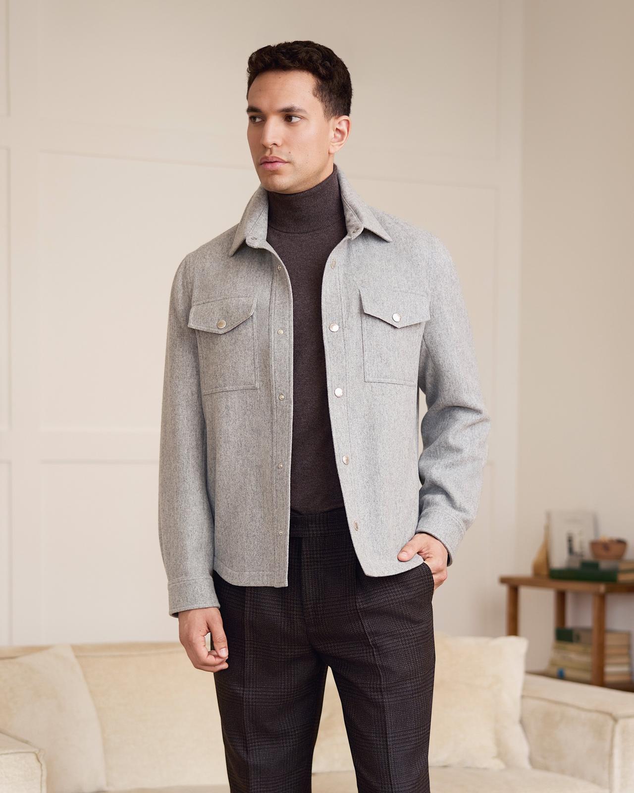 A male model wearing a light grey Brunello Cucinelli cashmere overshirt, brown turtle neck shirt and paired with dark grey check wool suit pants