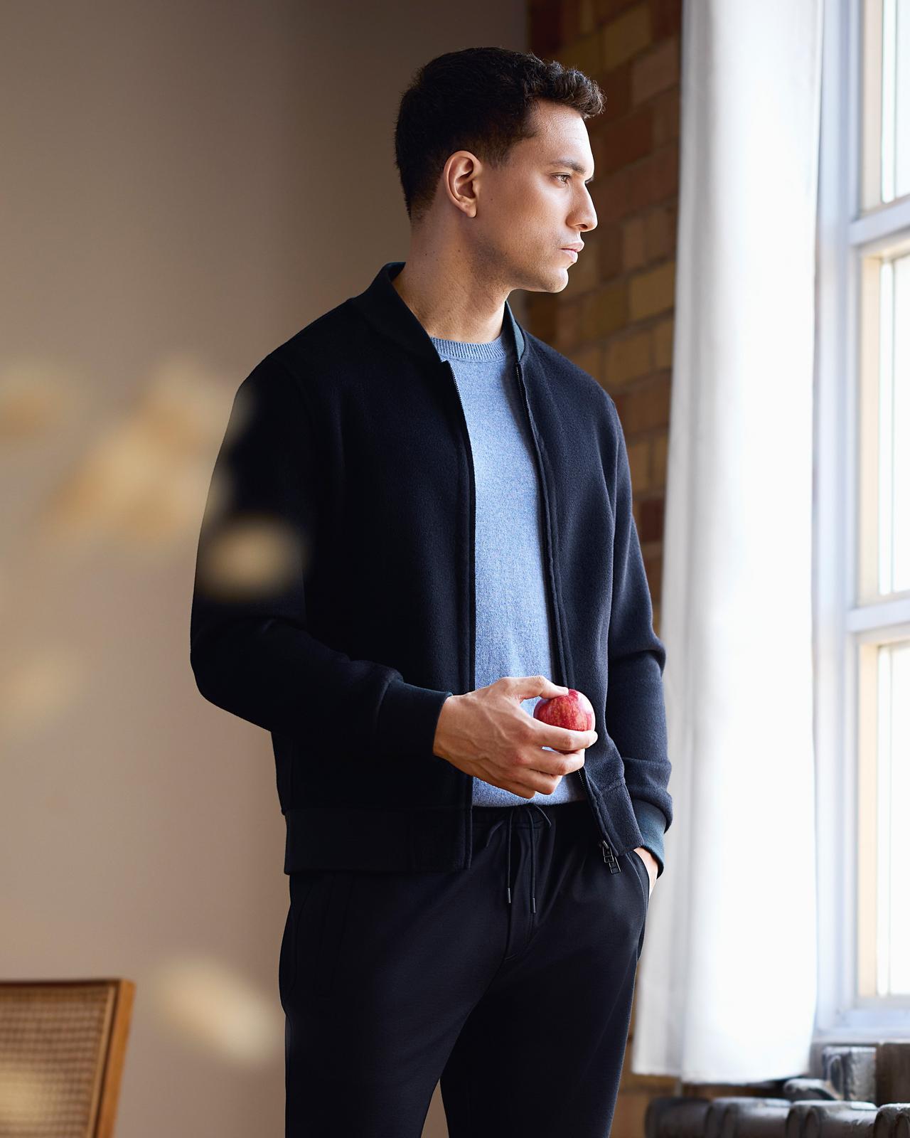 A male model wearing a navy wool bomber, light blue crewneck shirt, and navy joggers