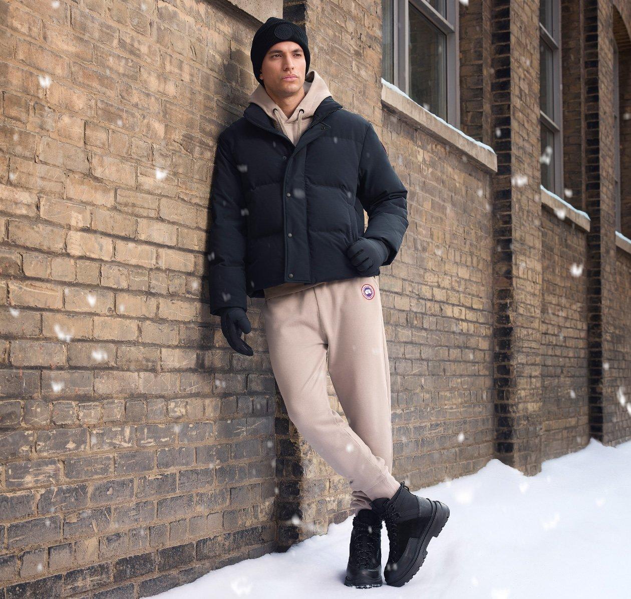 A male model wearing a brown lightweight jacket, paired with a cream colored zip-up knit sweater, white casual shirt, and striped navy tie