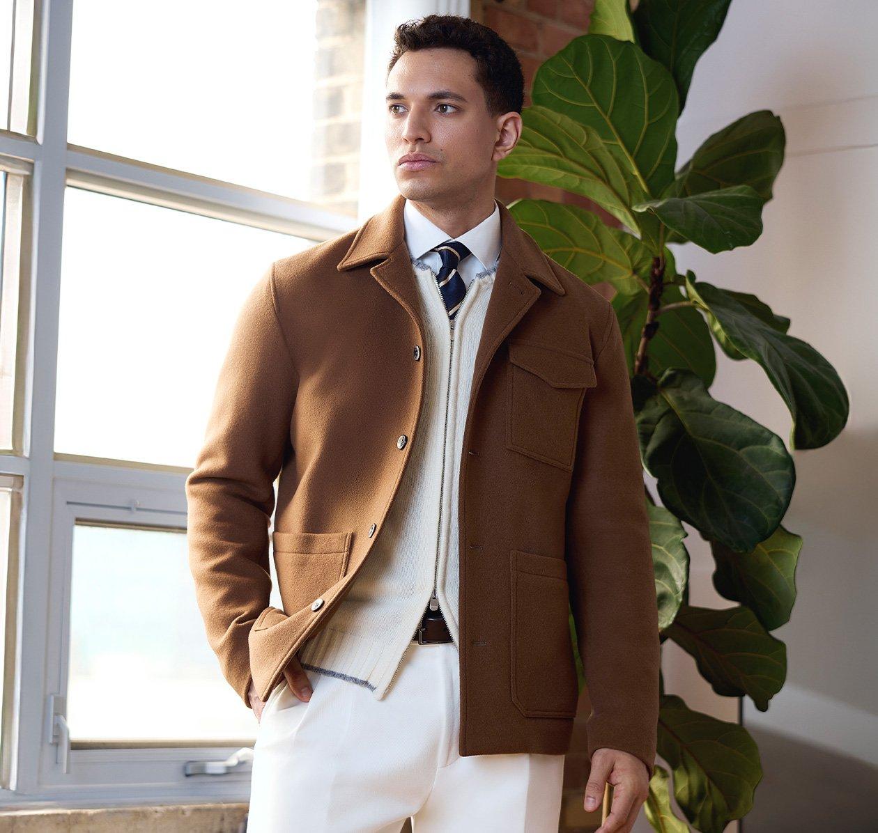 Un mannequin masculin porte une veste légère brun clair, assortie d’un chandail en tricot à fermeture éclair couleur crème, d’une chemise blanche décontractée et d’une cravate bleu marine à rayures