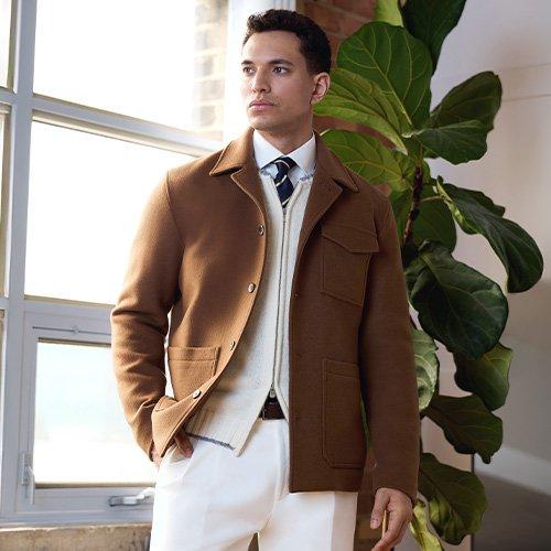 Un mannequin masculin porte une veste légère brun clair, assortie d’un chandail en tricot à fermeture éclair couleur crème, d’une chemise blanche décontractée et d’une cravate bleu marine à rayures