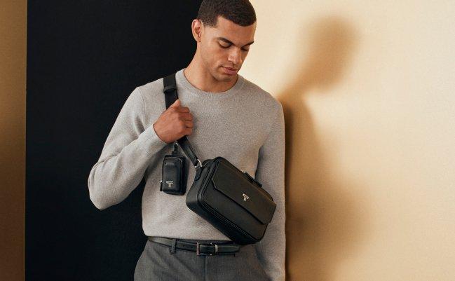 Un homme portant un t-shirt gris tenant un sac de voyage latéral de Tumi