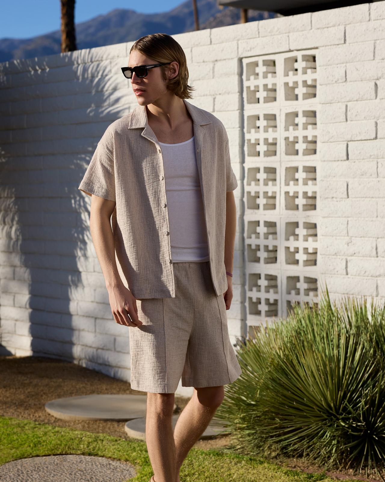 un homme en short et lunettes de soleil debout devant un mur