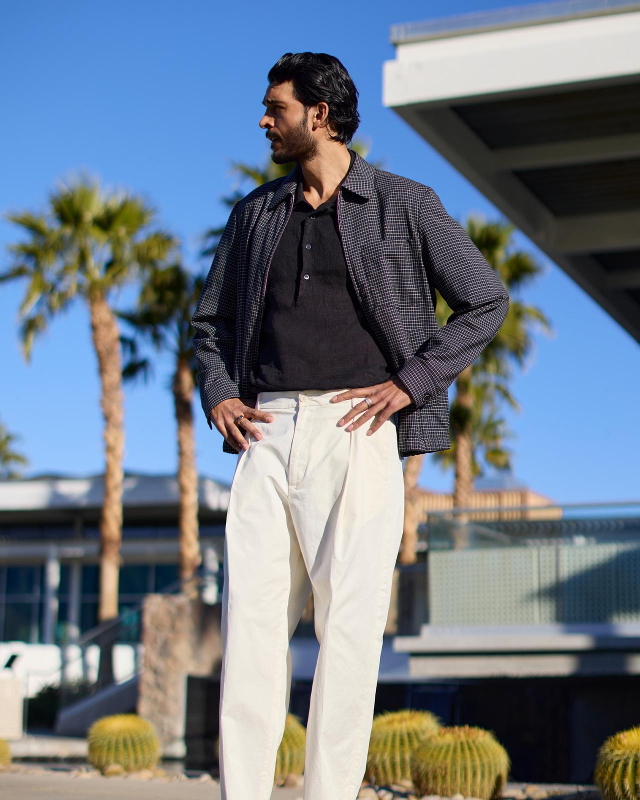 a man in a navy jacket and polo with white pants in front of palm trees