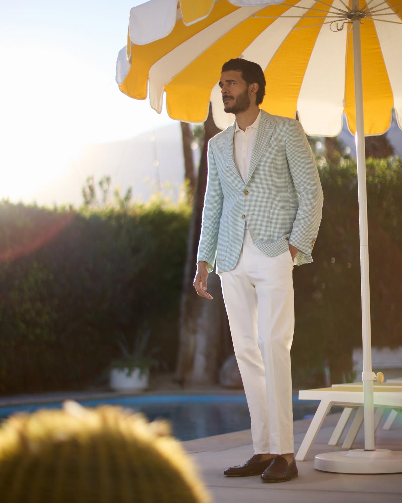 a man in a blue sport jacket and white pants under a beach umbrella