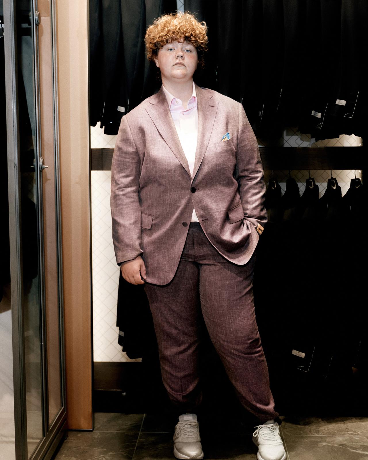 a person in a suit standing in front of a rack of clothes