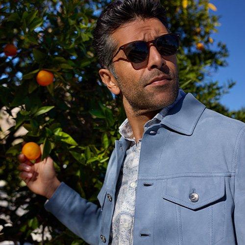 A man wearing sunglasses picking an orange