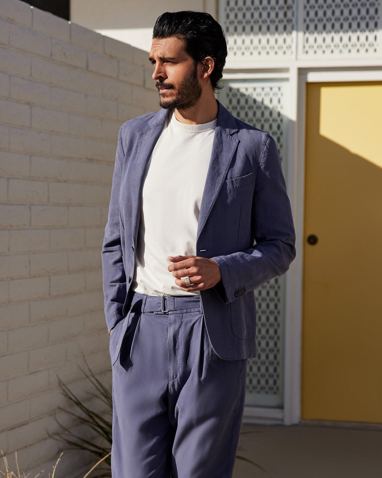 a man in a suit and white t-shirt standing outside in front of a building