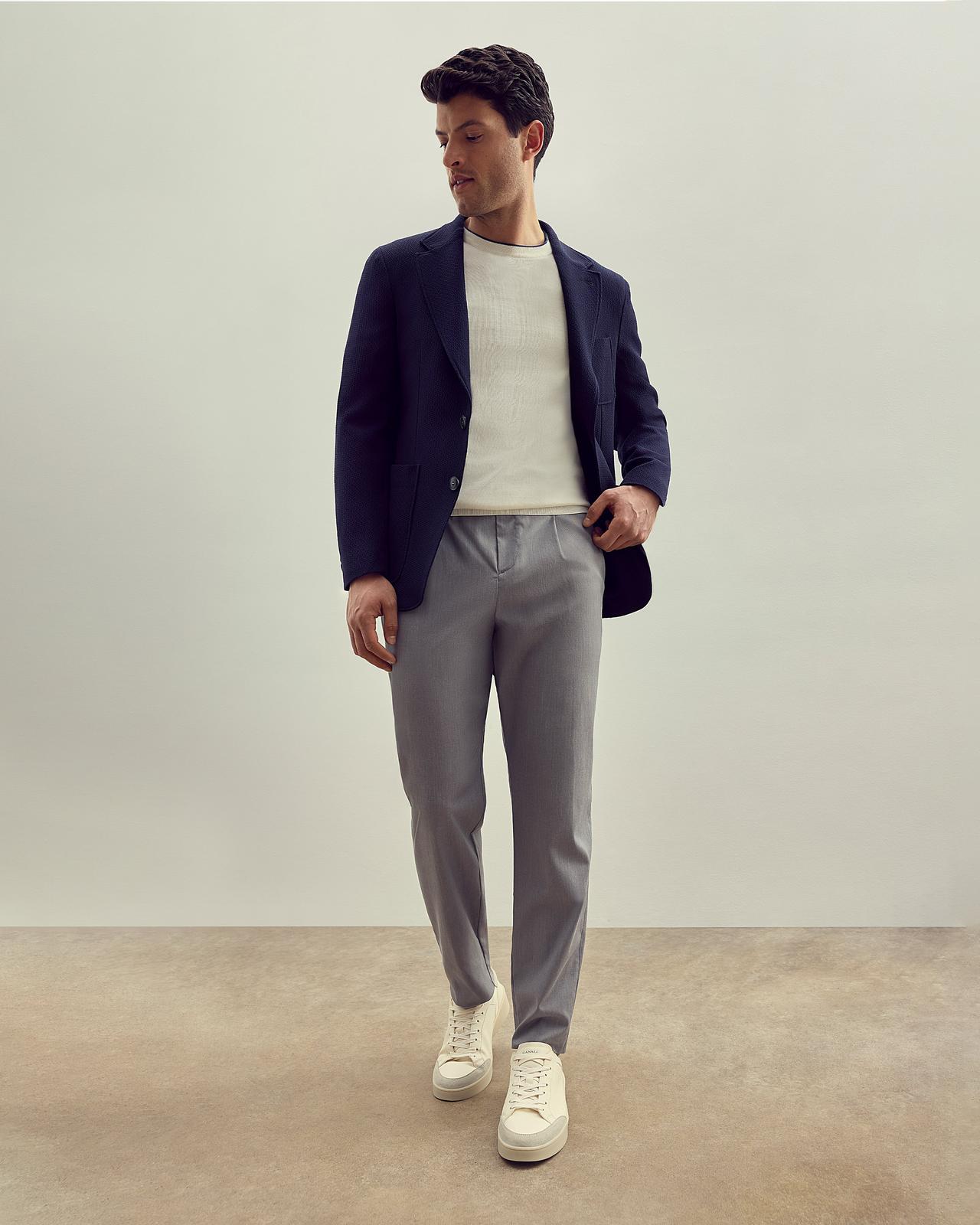 un modèle masculin en pantalon gris, un t-shirt blanc et une veste de sport bleu marine