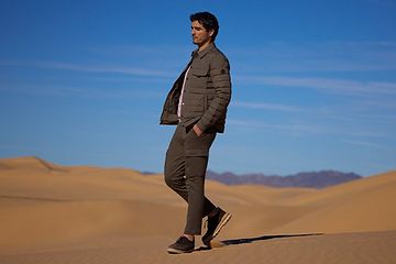 A man walking on a desert sand dune in a jacket