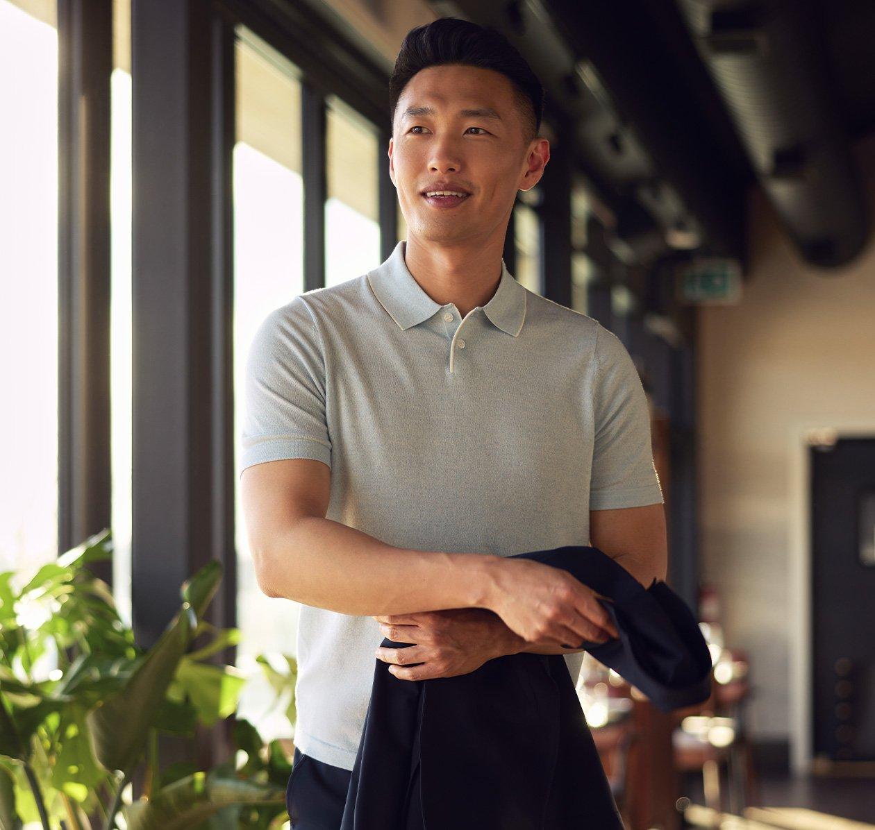 Male model in blue polo holding a jacket