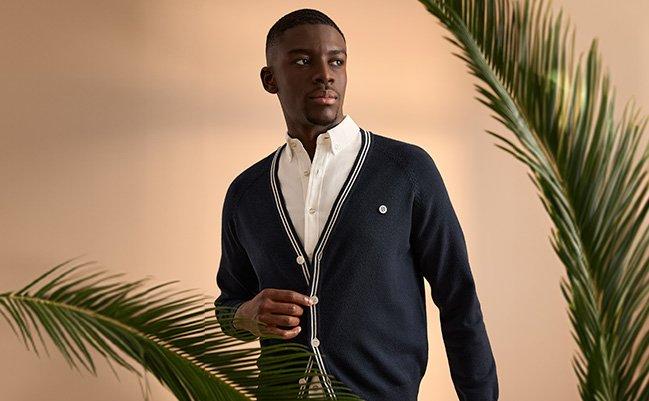 A man wearing a dark blue lightweight sweater and knit layered over a white shirt