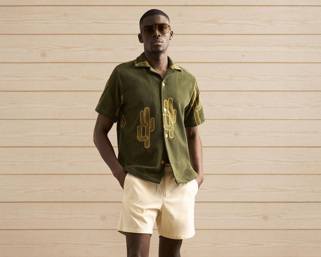 Un homme portant une chemise verte décontractée à motif de cactus et un short beige.