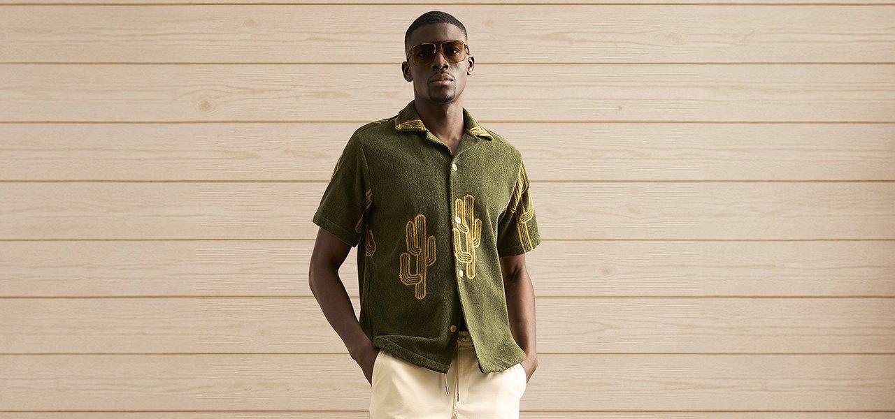A man wearing a green casual shirt with cactus pattern and beige shorts