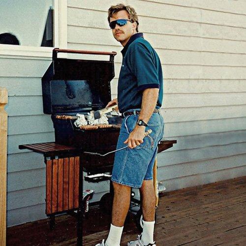 A dad using the barbecue wearing jean shorts and blue casual shirt