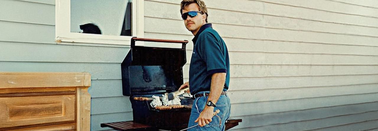 Un homme portant un short en jean et une chemise bleue décontractée fait un barbecue