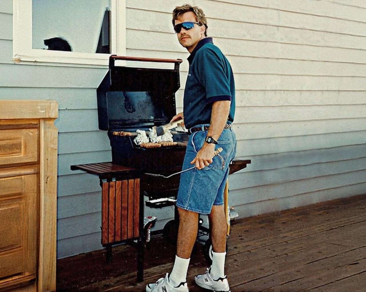 Man wearing jean shorts a blue casual shirt barbecuing