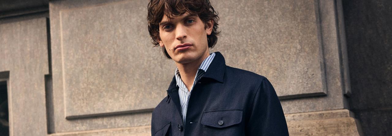 A man wearing a navy blue overshirt with white and blue striped shirt
