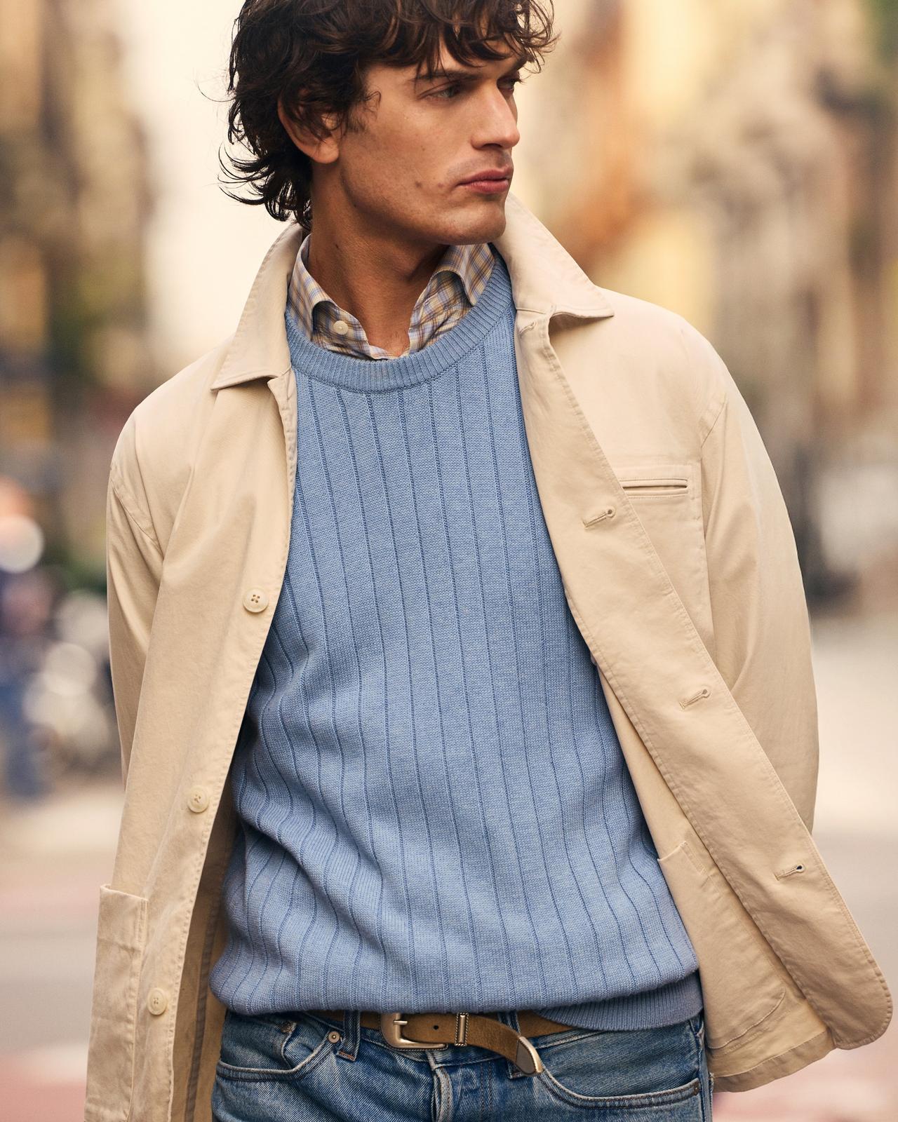 A man wearing a beige overshirt with light blue sweater and check patterned shirt 