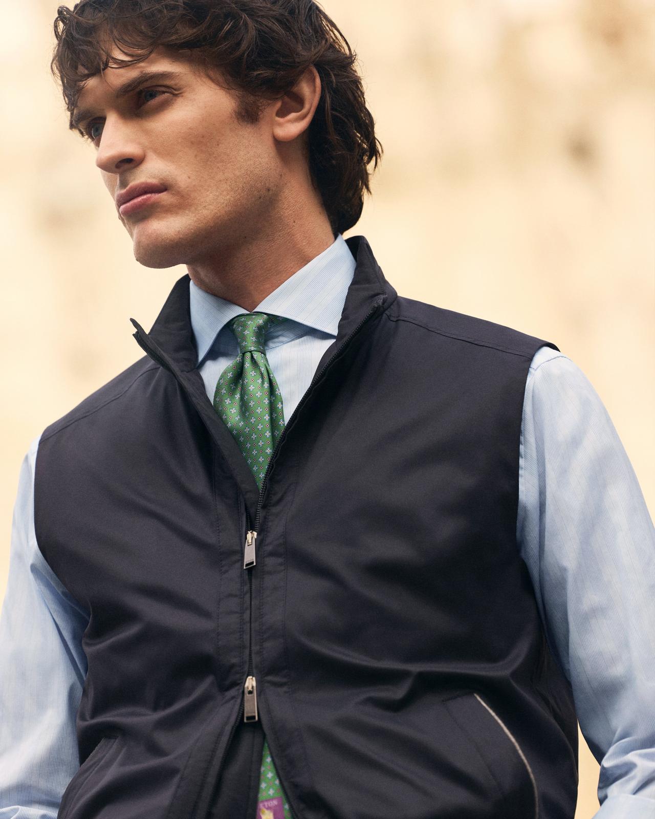 A man wearing a dark blue jacket with light blue shirt and green star patterned tie