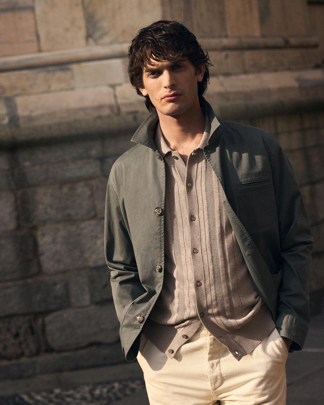A man wearing a light grey-brown overshirt with beige buttoned sweater