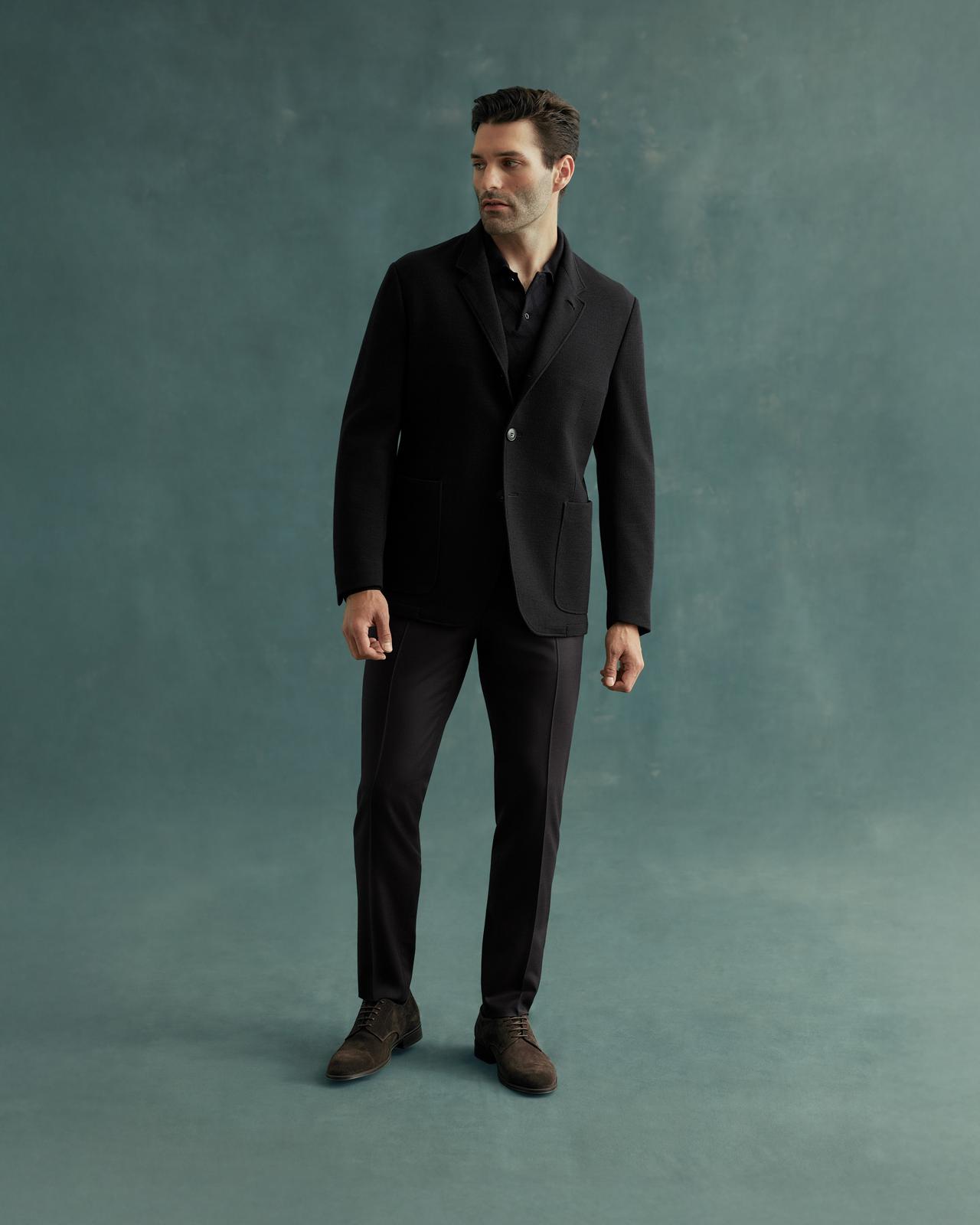 A man wearing a black Canali blazer over a black shirt and black pants with black dress shoes