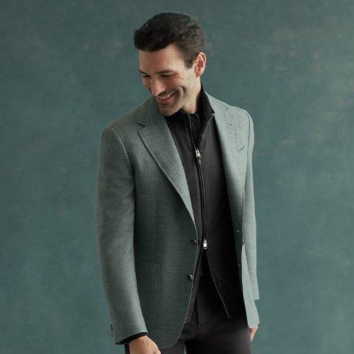 A man wearing a green Canali blazer over a black shirt and black pants with black dress shoes