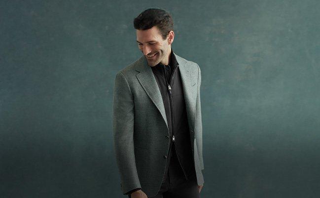 A man wearing a green Canali blazer over a black shirt and black pants with black dress shoes