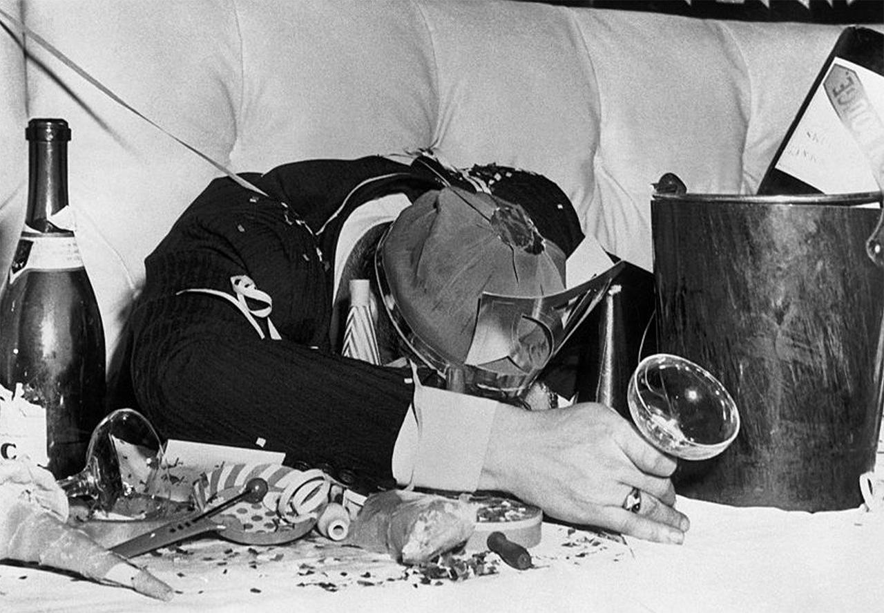 Personne affaissée sur une table de fête en désordre avec des bouteilles de champagne