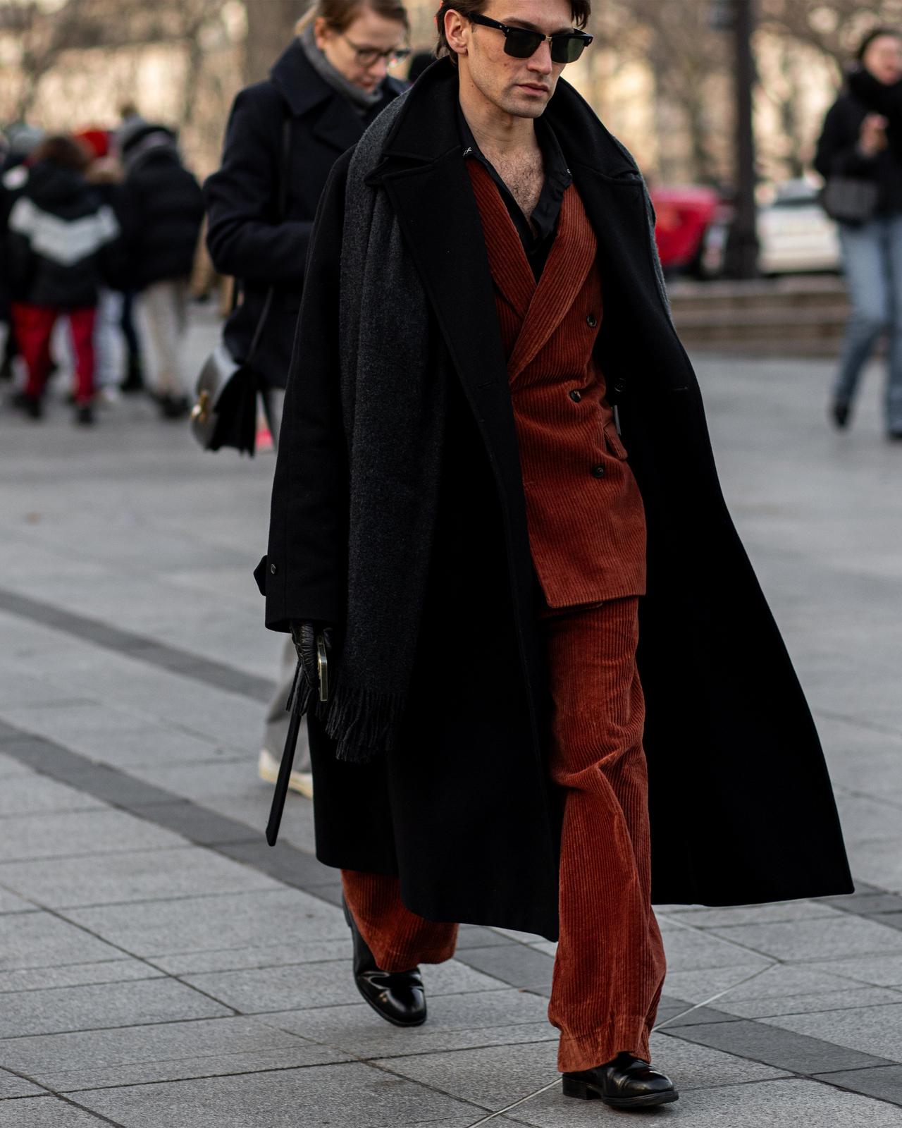 A man in a red suit and black coat walking down a street