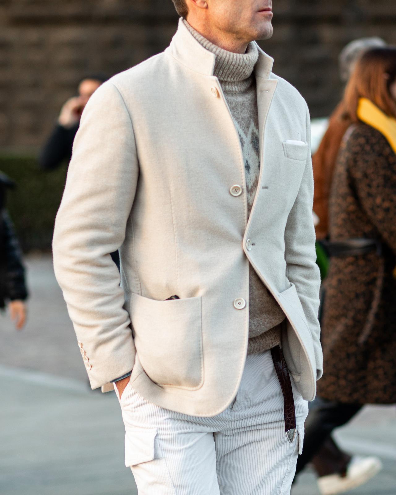 A man in a white jacket and white pants walking down a street