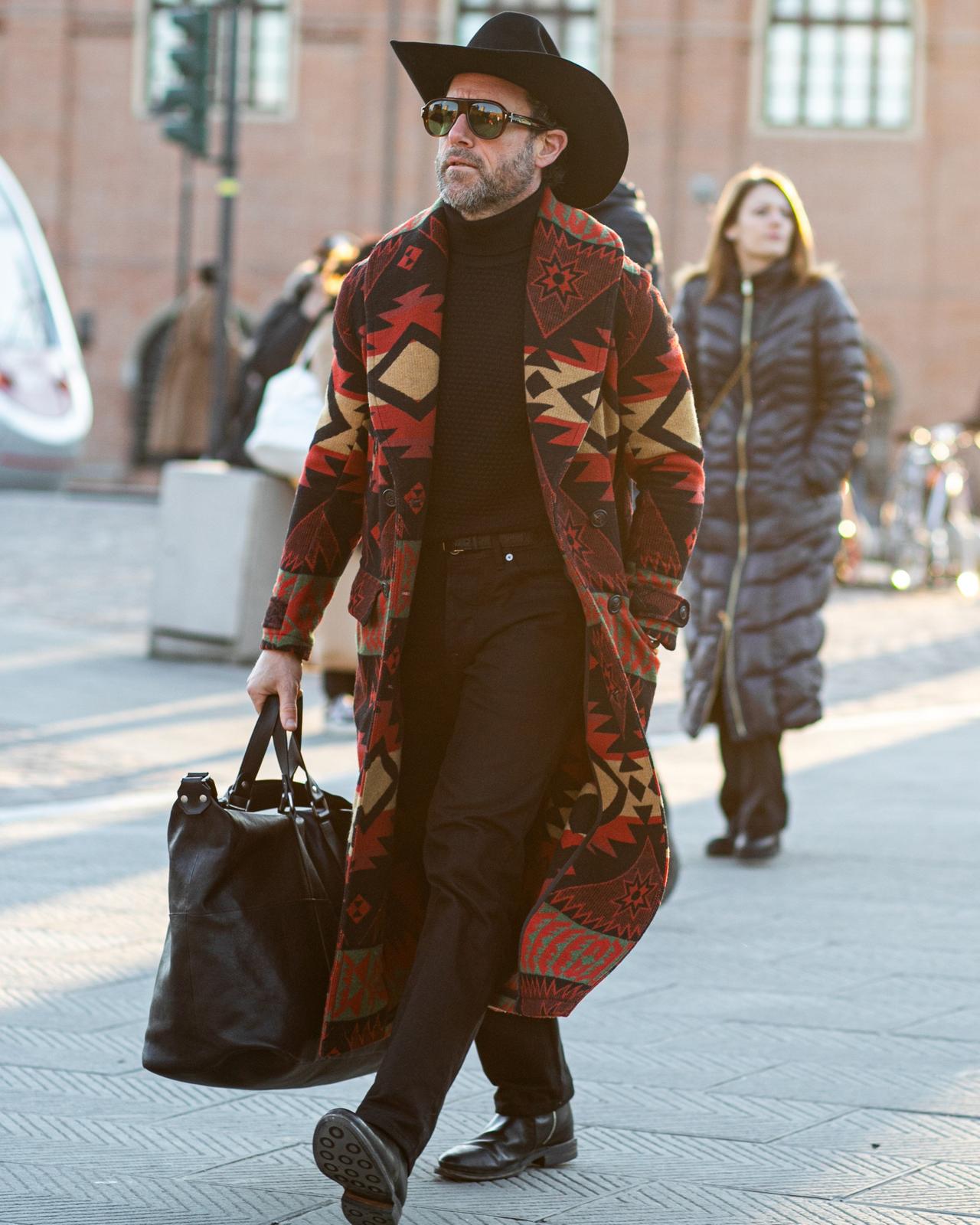 Un homme au chapeau de cowboy marchant dans une rue avec un sac