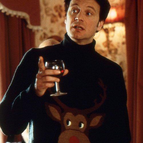 Colin Firth in Movie Still: Talking in Ugly Christmas Sweater, Dark Green with Reindeer Graphic, Red Wine in Hand
