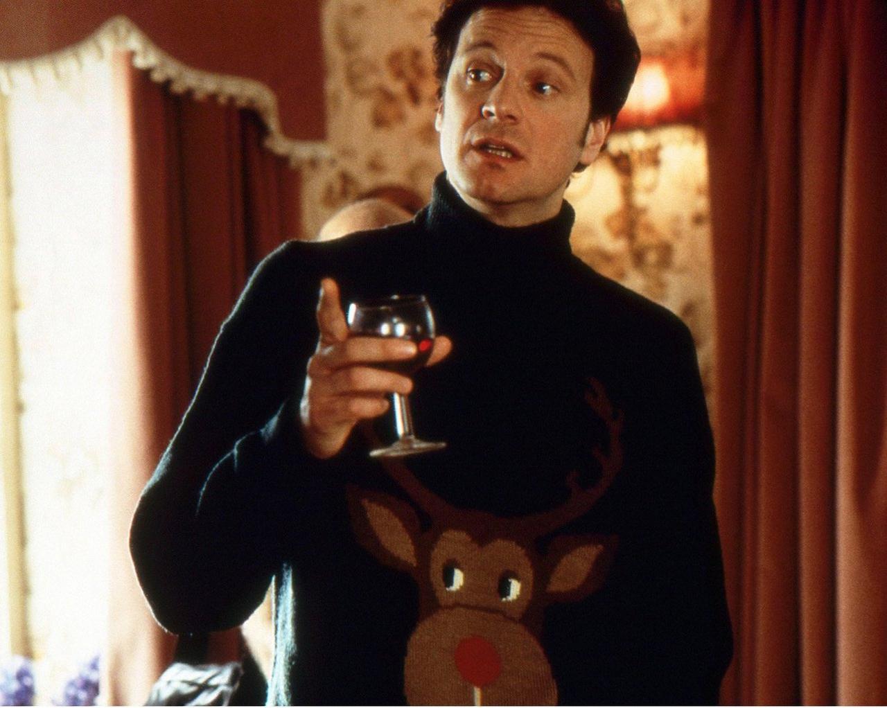 Colin Firth in Movie Still: Talking in Ugly Christmas Sweater, Dark Green with Reindeer Graphic, Red Wine in Hand