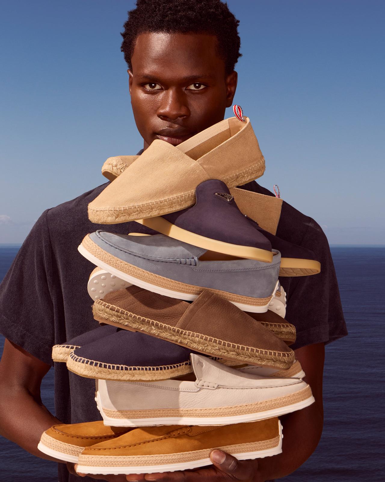 A man holding a stack of shoes in front of the ocean.