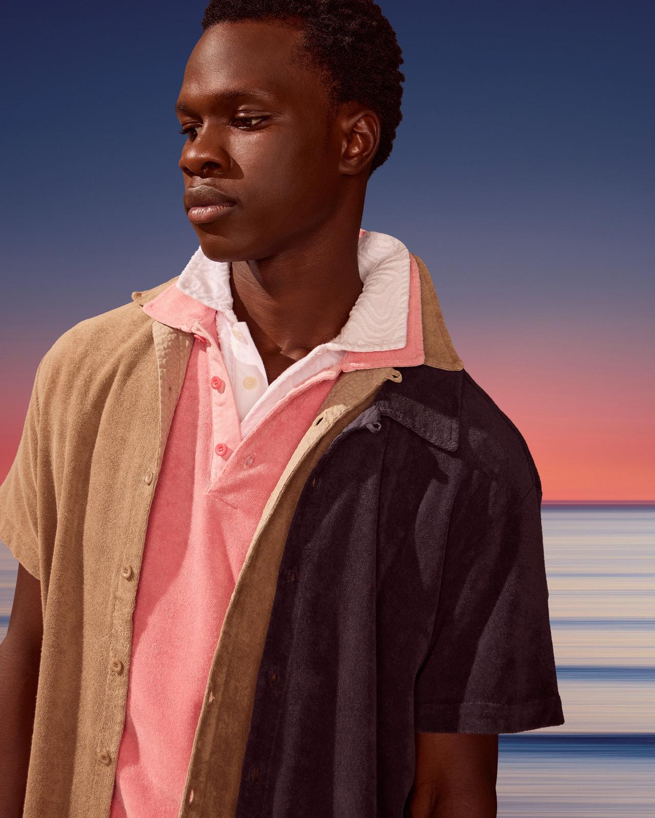 A man standing in front of a sunset wearing a pink shirt and a brown shirt.